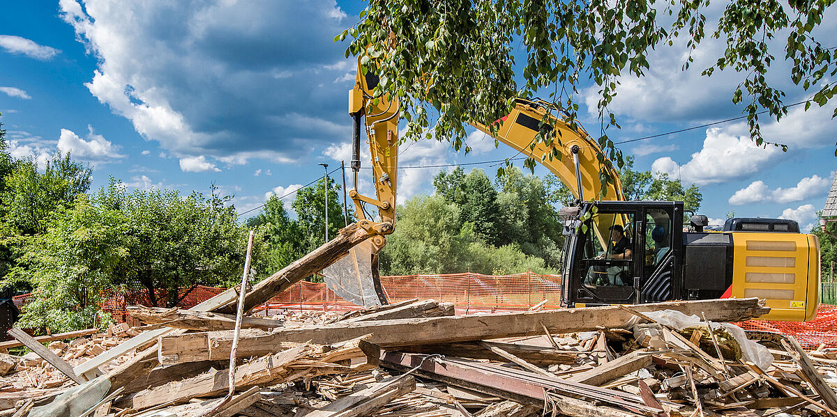 Side view of an excavator digging through rubble at a demolition site.